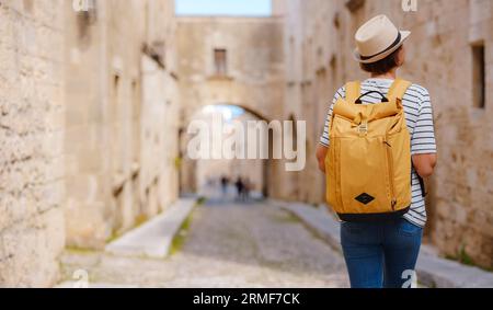 Sommerausflug zur Insel Rhodos, Griechenland. Junge Asiatin in gestreiftem T-Shirt und Hut wandelt in der Straße der Ritterburg. Weibliche Reisende Stockfoto