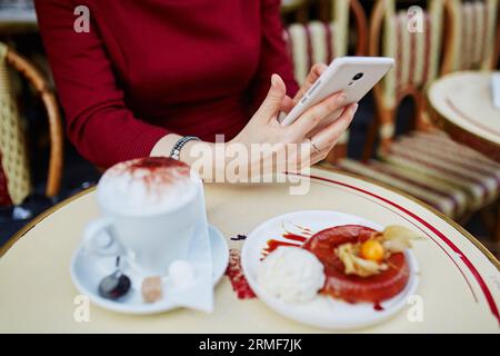 Französische Frau trinkt Kaffee in einem Café im Freien in Paris, Frankreich, und verwendet ihr Handy für SMS, Browsen oder Fotos. Nahaufnahme der Hände, die Gadg halten Stockfoto