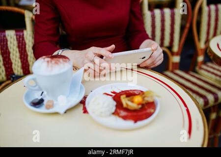 Französische Frau trinkt Kaffee in einem Café im Freien in Paris, Frankreich, und verwendet ihr Handy für SMS, Browsen oder Fotos. Nahaufnahme der Hände, die Gadg halten Stockfoto