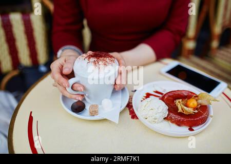 Französische Frau trinkt Kaffee in einem Café im Freien in Paris, Frankreich, und verwendet ihr Handy für SMS, Browsen oder Fotos. Nahaufnahme der Hände, die Gadg halten Stockfoto