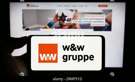 Person mit Handy mit Logo der Wüstenrot Württembergischen AG (WW) auf dem Bildschirm vor der Webseite. Konzentrieren Sie sich auf das Display des Telefons. Stockfoto