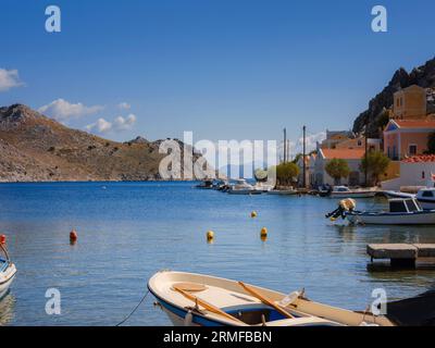 Blick auf den Hafen von Symi oder Simi, klassische Schiffsyachten, Häuser auf Inselhügeln, ägäische Meeresbucht. Griechenland Inseln Urlaub Urlaub Reisen Touren Stockfoto