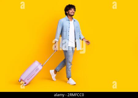 Foto in voller Länge von fröhlich positivem Mann gekleidete Jeansjacke Wanderurlaub Leere Raum isolierte gelbe Farbe Hintergrund Stockfoto