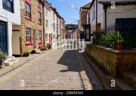 Staithes, England – 24. Mai 2023: Eine gepflasterte Straße und alte Reihenhäuser entlang der Staithes High Street in North Yorkshire. Stockfoto