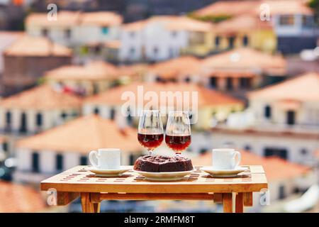 Zwei Gläser Madeira-Wein, zwei Tassen frischer Espresso-Kaffee und traditioneller portugiesischer Honig- und Nussdessert Bolo de mel im Café mit Blick auf Funch Stockfoto