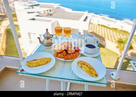 Köstliches Frühstück mit Omelette, Gebäck, Kaffee und Minztee auf dem Balkon mit Meerblick im marokkanischen Hotel Stockfoto