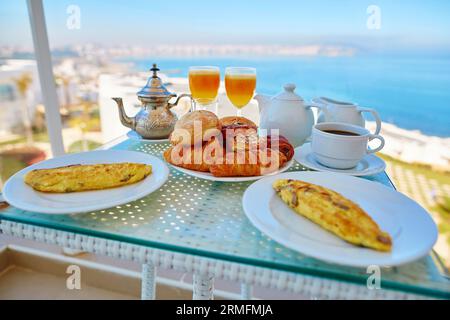 Köstliches Frühstück mit Omelette, Gebäck, Kaffee und Minztee auf dem Balkon mit Meerblick im marokkanischen Hotel Stockfoto