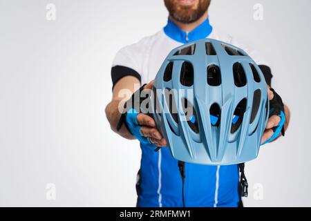 Nicht erkennbarer bärtiger Radfahrer, der modernen Helm vor der Kamera zeigt. Nahaufnahme des Schutzhelms, dargestellt von Mann im Fahrradkit, isoliert auf weiß Stockfoto