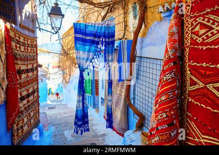 Viele bunte marokkanische Teppiche zum Verkauf auf einer Straße in Medina von Chefchaouen, Marokko, einer kleinen Stadt im Nordwesten Marokkos, die für ihre blauen Gebäude bekannt ist Stockfoto