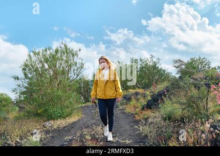 Glückliche junge Wanderin, die auf dem schwarzen Sand des Lavasteins des Ätna spaziert, die Freiheit genießt und den Panoramablick genießt. Stockfoto