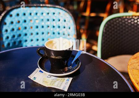 Leere Tasse schwarzen Kaffee und 5-Euro-Banknote auf einem Tisch im Freien Café in Paris, Frankreich Stockfoto