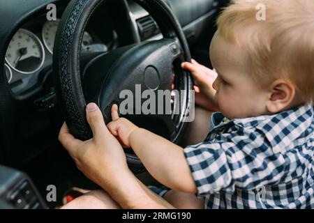 Papa zeigt seinem kleinen Sohn, wie er das Auto fährt, während er hinter dem Steuer sitzt Stockfoto