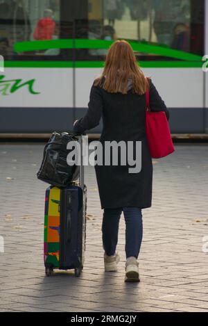 Junge, rothaarige, coucasische Frauen, mit Koffer und Taschen, eilig, rechtzeitig für den lokalen Bus zu kommen, um auf Urlaub oder Geschäftsreise zu gehen. Stockfoto