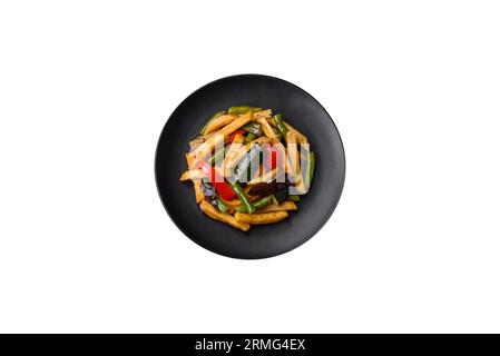 Köstliche Bratkartoffeln mit Paprika, Spargelbohnen, Salz und Gewürzen auf einem Teller mit dunklem Betonhintergrund Stockfoto