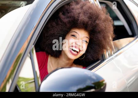Porträt einer jungen afroamerikanischen Frau in lässigem Tuch mit Afro-Haar lächelnd und Blick auf die Kamera beim Autofahren Stockfoto