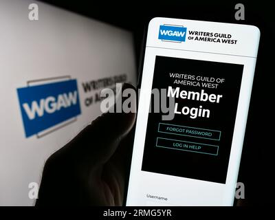 Person, die ein Mobiltelefon mit Webseite der Labor union Writers Guild of America West (WGAW) auf dem Bildschirm mit Logo hält. Konzentrieren Sie sich auf die Mitte der Telefonanzeige. Stockfoto