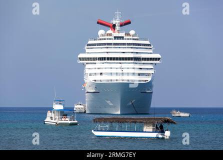 Der Blick am Morgen auf ein großes Kreuzfahrtschiff, umgeben von kleinen verschiedenen Booten in der Nähe der Insel Grand Cayman (Cayman Islands). Stockfoto