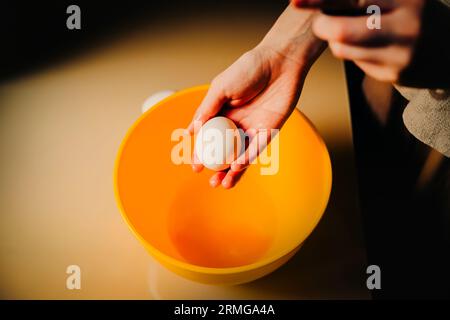 Eine Frau hält ein Hühnerei in der Hand über einer Schüssel, während sie sich darauf vorbereitet, es zu kochen. Die Hausmannskost und die Zubereitung von Mahlzeiten von Grund auf Stockfoto