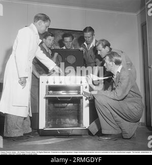 In den 1950er Jahren Ein Mann bei einem Elektrokocher des schwedischen Herstellers Husqvarna, der einen weißen Mantel trägt, weist eine Gruppe von Soldaten auf die Details und Merkmale des neuen Ofens hin. Schweden 1950. Kristoffersson ref AZ69-10 Stockfoto