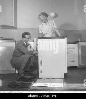 In den 1950er Jahren Ein Mann bei einem Elektrokocher des schwedischen Herstellers Husqvarna, der etwas repariert. Eine Frau steht auf der Seite und schaut. Schweden 1950. Kristoffersson ref AZ69-12 Stockfoto