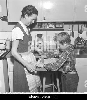 Backen in den 1950er Jahren Eine Mutter mit ihrem Sohn in der Küche. Er hilft ihr beim Backen und rollt den Teig auf einem ausziehbaren Tischbrett. Schweden 1958 Kristoffersson ref BY20-6 Stockfoto