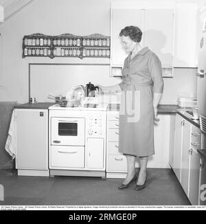 In den 1950er Jahren Eine Frau in einer typischen Küche aus den 1950er Jahren mit Holzschränken und Gewürzen auf Regalen über dem Herd. Sie hält eine Kaffeekanne im typischen emaillierten Look der 50er Jahre. Schweden 1959. Kristoffersson ref CL8-9 Stockfoto