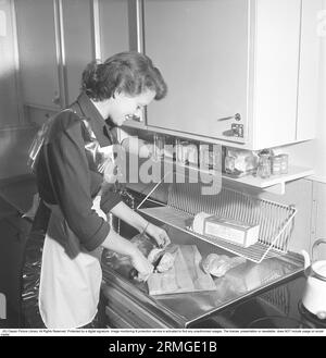 In der Küche der 1950er Das Innere einer Küche und eine junge Frau, die am Spülbecken steht und die Zutaten zubereitet. Sie trägt eine Plastikschürze. Sie ist Haide Göransson, 1928–2008, Modemodel und Schauspielerin. Schweden 1950 Kristoffersson ref AU23-2 Stockfoto