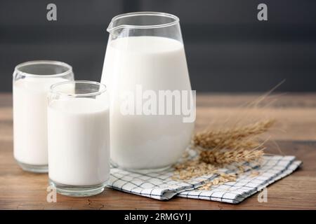 Gläser und Kanne mit frischer Milch und Weizenohren auf Holztisch Stockfoto