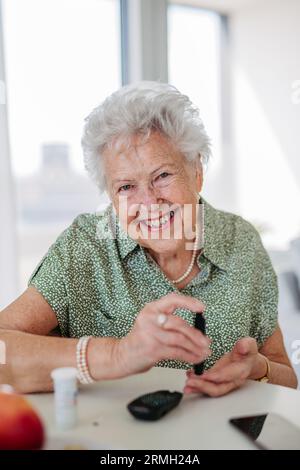 Porträt einer diabetischen Seniorenpatientin, die ihren Blutzuckerspiegel mit einem Blutzuckermessgerät mit Fingerstick-Test überprüft. Stockfoto