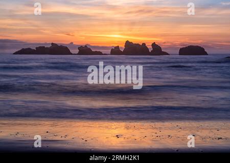 Der bunte Himmel thront hinter Meeresstapeln, hinter langen Wellen am Bandon Beach in Bandon, Oregon Stockfoto