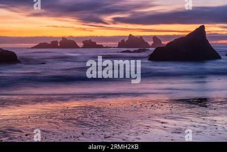 Nasser Sand sieht metallisch aus, da er einen farbenfrohen Nachthimmel mit weichen, langen Wellen am Bandon Beach in Bandon, Oregon, reflektiert Stockfoto