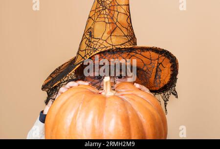Halloween-Feiertagsfeier. Junge in Hexenhut versteckt von halloween Kürbis. Halloween-Kind mit magischem Hut. Kleinkind spielt Trick oder Belohnung. Kleines Kind Stockfoto