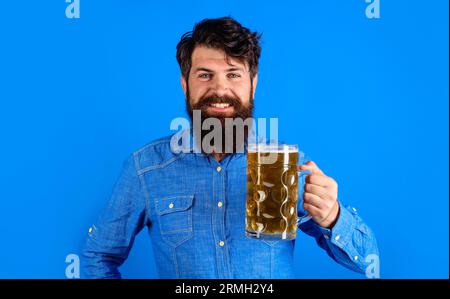 Bierzeit. Lächelnder bärtiger Mann mit Craft-Bier in einer Tasse in Bar oder Pub. Deutsche Tradition. Oktoberfest. Stylischer Mann im Jeanshemd trinkend Stockfoto