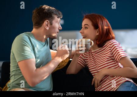 Glückliches Paar Mann Frau trinkt Tee sprechend lächelnd sitzend auf Couch zu Hause. Stockfoto