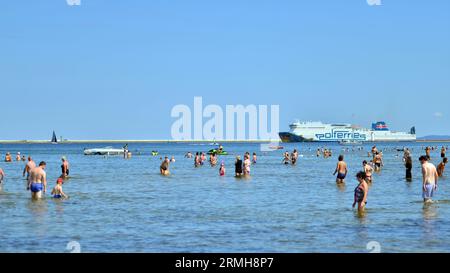 Swinoujscie, Polen. August 2023. Leute, die am Strand baden. Im Hintergrund die Cracovia Ferry des Fährbetreibers Polferries Stockfoto