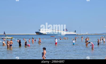 Swinoujscie, Polen. August 2023. Leute, die am Strand baden. Im Hintergrund die Cracovia Ferry des Fährbetreibers Polferries Stockfoto