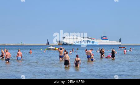 Swinoujscie, Polen. August 2023. Leute, die am Strand baden. Im Hintergrund die Cracovia Ferry des Fährbetreibers Polferries Stockfoto