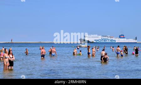 Swinoujscie, Polen. August 2023. Leute, die am Strand baden. Im Hintergrund die Cracovia Ferry des Fährbetreibers Polferries Stockfoto