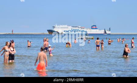 Swinoujscie, Polen. August 2023. Leute, die am Strand baden. Im Hintergrund die Cracovia Ferry des Fährbetreibers Polferries Stockfoto