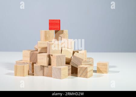 Roter Würfel, der auf einem Haufen aus hellen Holzwürfeln steht, Konzept für Geschäft, Karriere und Erfolg, grauer Hintergrund mit Kopierraum Stockfoto