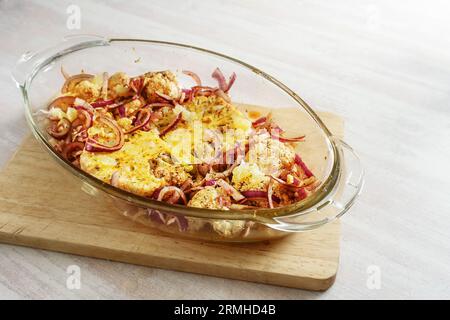 Scharf gebackene Blumenkohlsteaks mit roten Zwiebeln in einem Glasauflauf auf einem hölzernen Küchenbrett auf einem hellen Tisch, vegetarisches Gemüsegericht, Kopierraum, Stockfoto