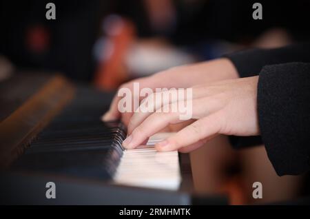 Nahaufnahme von Händen und Fingern, die eine Tastatur oder weiße Klaviertasten spielen. Publikum verschwommen im Hintergrund. Linke Hand im Fokus Stockfoto