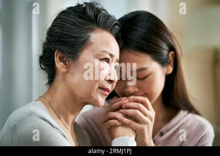 Junge asiatische Erwachsenentochter tröstet Seniormutter mit psychischer Erkrankung Stockfoto