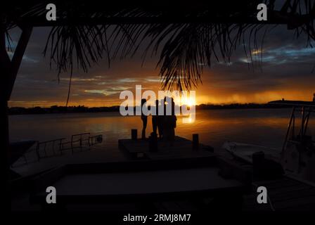 Die Silhouetten von 4 Personen, die bei Sonnenuntergang auf der Insel Ambergris Caye in Belize, Mittelamerika, auf einem Pier stehen. Stockfoto