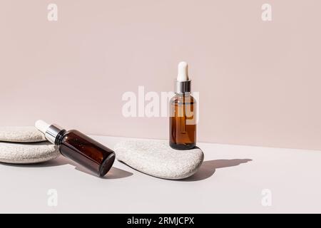 Zwei Kosmetikflaschen mit Bio-Naturpflege. Der eine steht, der andere liegt auf grauen Meeressteinen. Leerzeichen für Text. Beigefarbener Hintergrund Stockfoto