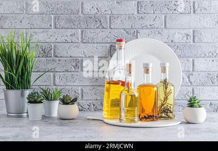 Verschiedene Glasölflaschen zum Kochen auf der Küchenarbeitsplatte. Kompakte Öllagerung. Blumen in Töpfen. Vorderansicht Stockfoto