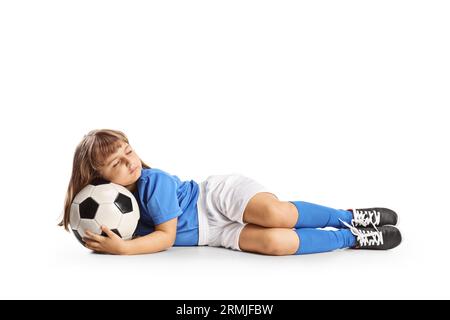 Kleines Mädchen in einem Fußballtrikot, das mit einem Ball isoliert auf weißem Hintergrund schläft Stockfoto