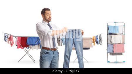 Mann, der eine Jeans vor trockenen Gestellen auf weißem Hintergrund hält Stockfoto