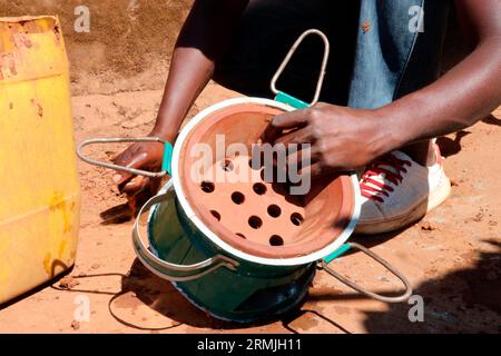 Ein Mann wird gesehen, wie er einen Holzkohleofen herstellt, der lokal als „Mbaula“ bekannt ist, in der Gemeinde Mtandile, Lilongwe. Der Holzkohleofen besteht aus Metall und Ton. Malawi. Stockfoto