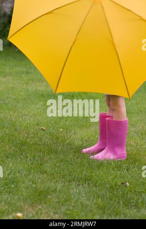 Junges Mädchen in rosa Stiefel unter gelben Regenschirm Stockfoto